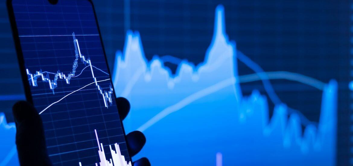 A person holding a phone in front of a stock chart