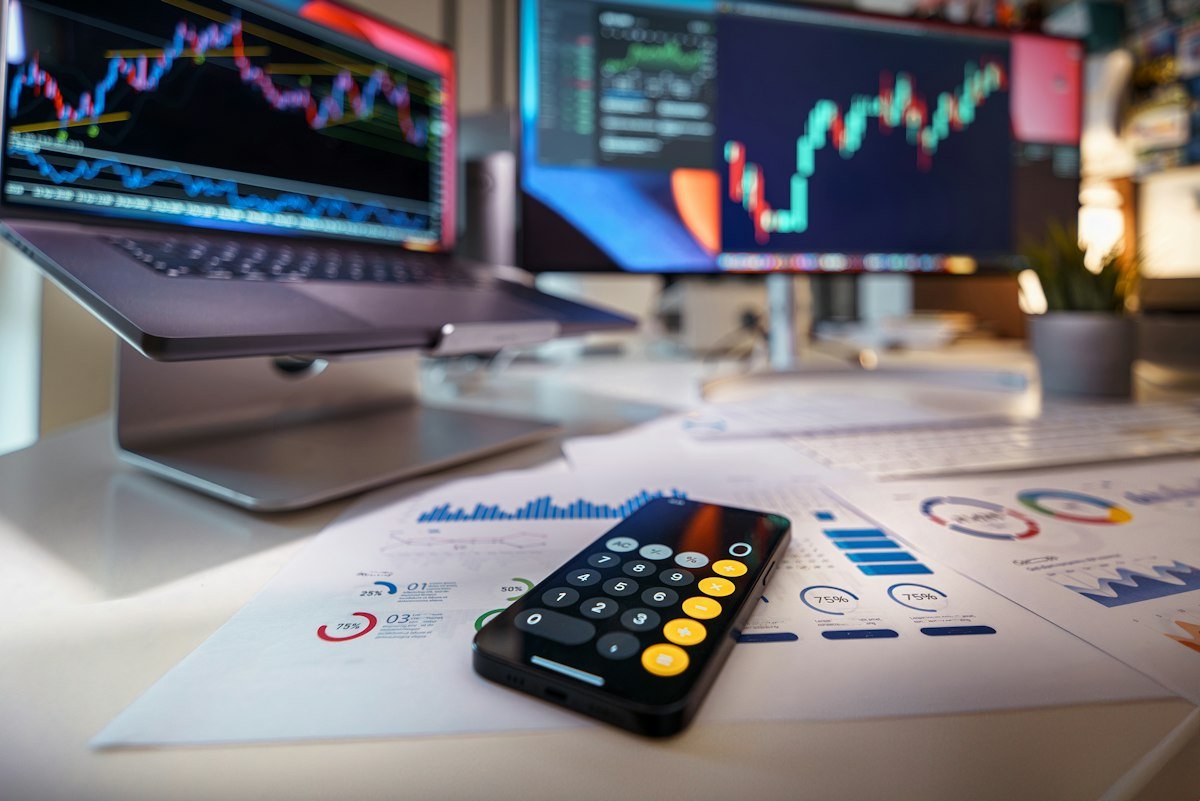 A smartphone calculator on a desk with financial charts